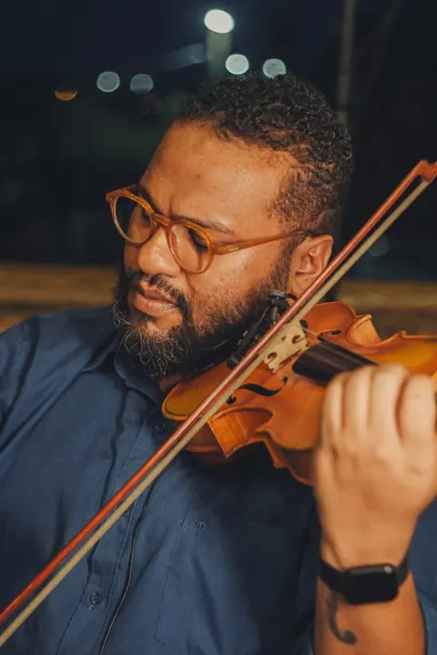 Violinista de óculos e barba tocando à noite, ao ar livre Violinista de óculos e barba tocando à noite, ao ar livre