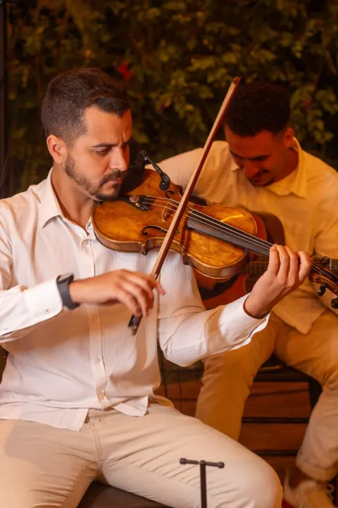 Violinista de camisa branca tocando ao ar livre, com outro músico ao fundo Violinista de camisa branca tocando ao ar livre, com outro músico ao fundo
